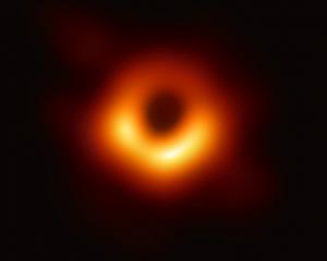 Abbildung eines schwarzen Lochs. Der Hintergrund des Bildes ist schwarz, in der Mitte ist ein rot-orangener Lichtring zu erkennen, der wiederum einen schwarzen Kreis in der Mitte hat.
